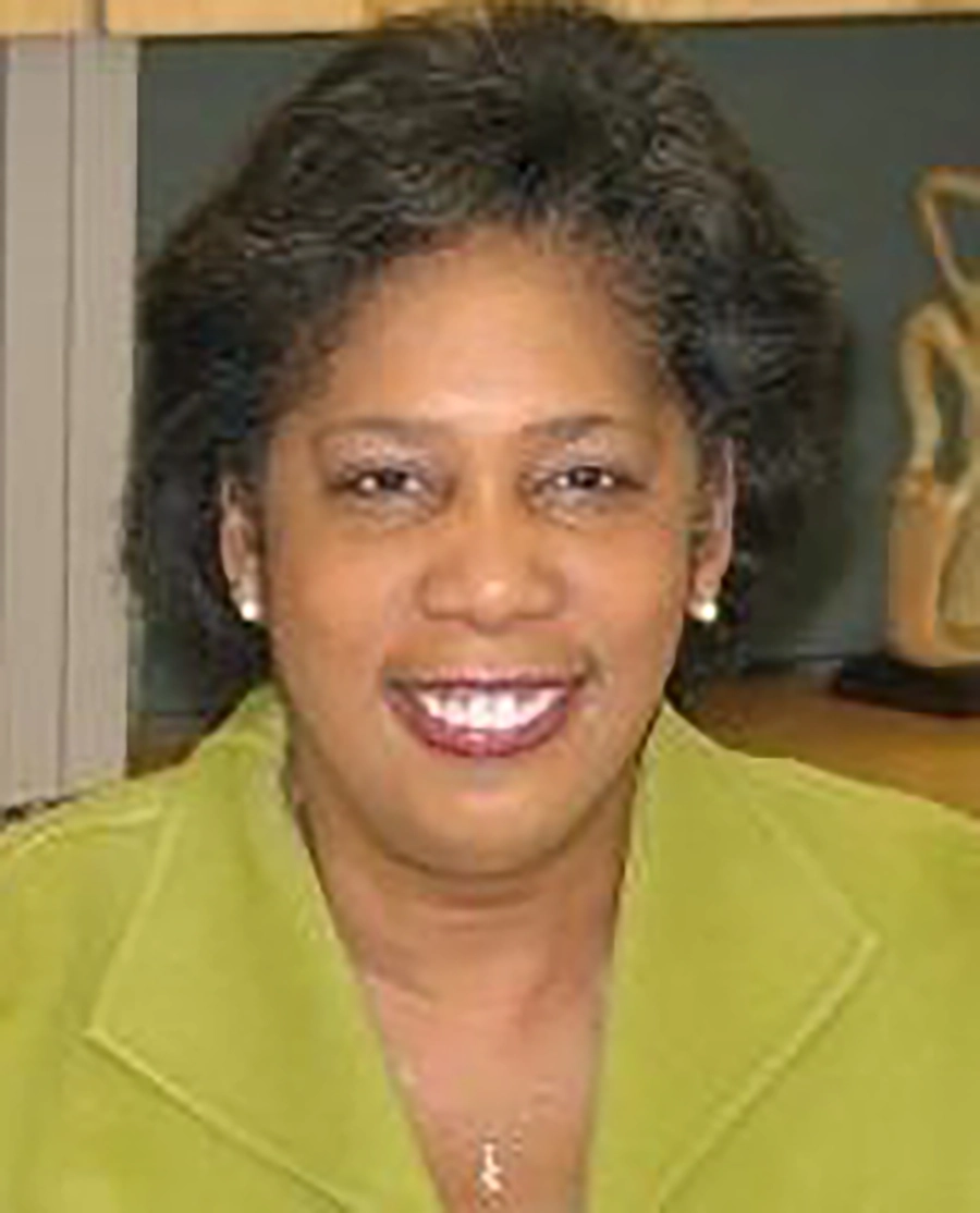 Close-up headshot of Deborah Sims, a smiling woman with dark, curly hair wearing a lime-green blazer and a small silver necklace