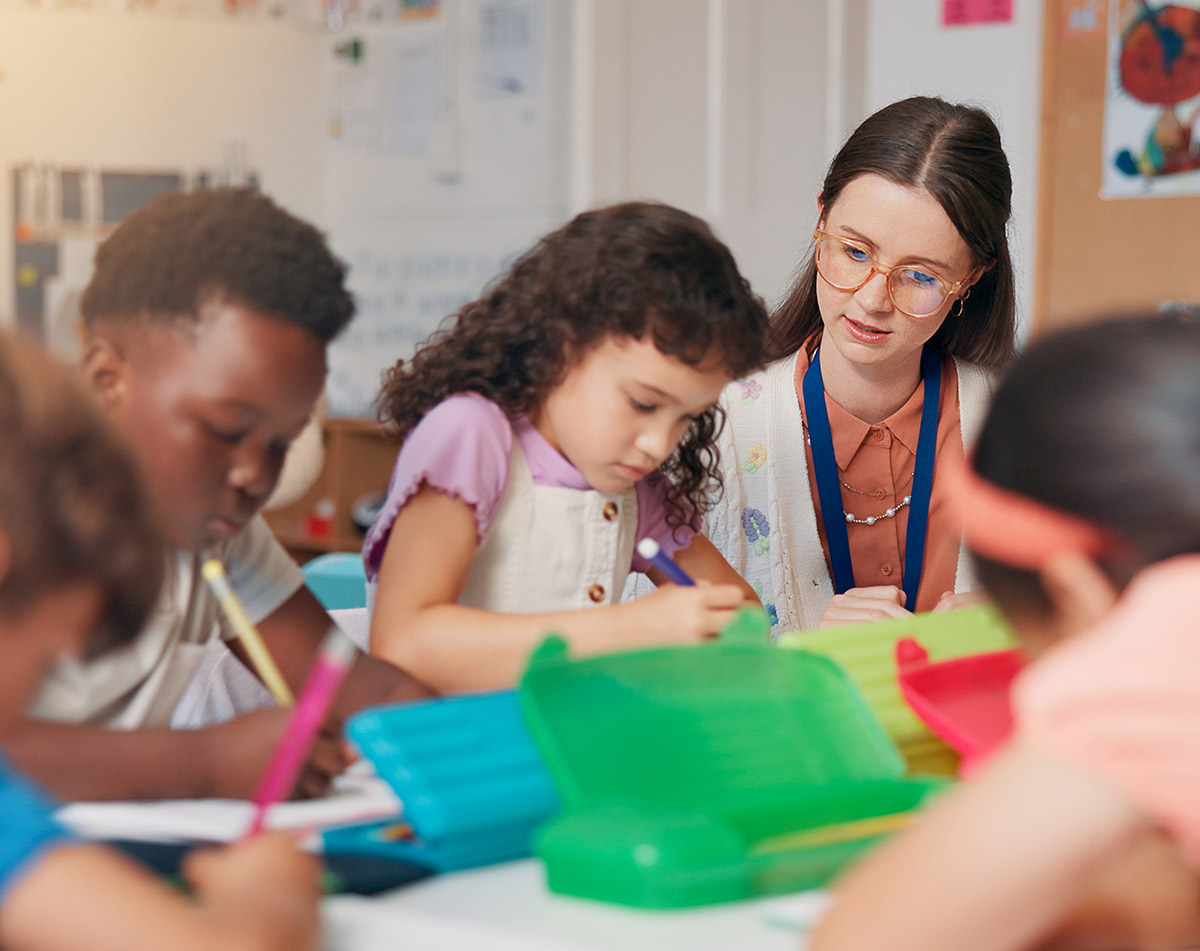 A candid shot of a diverse group of elementary students focused on their schoolwork while an educator provides personalized instruction