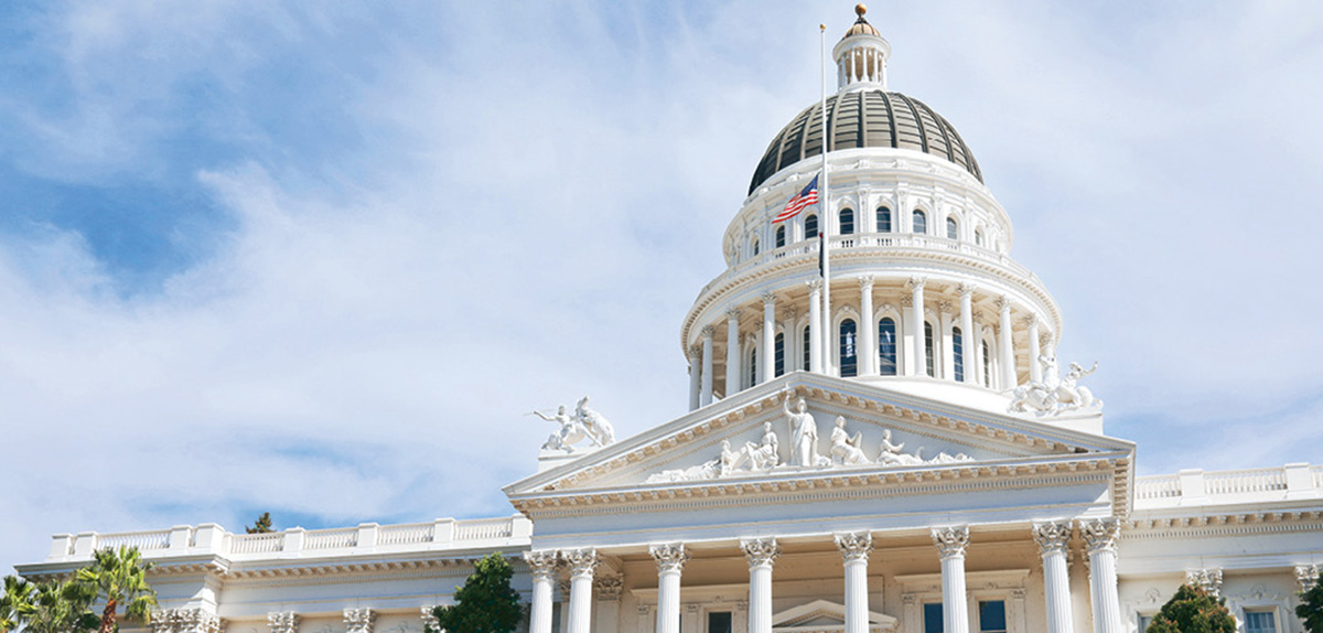 Exterior view of the California State Capitol building featuring its iconic white dome and neoclassical columns against a bright blue sky