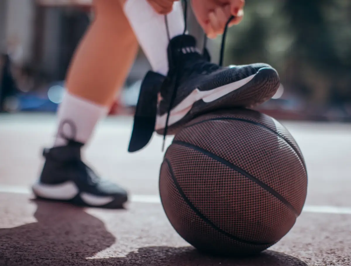 A close-up, low-angle shot of a basketball player's legs and feet on top of a basketball on an outdoor court