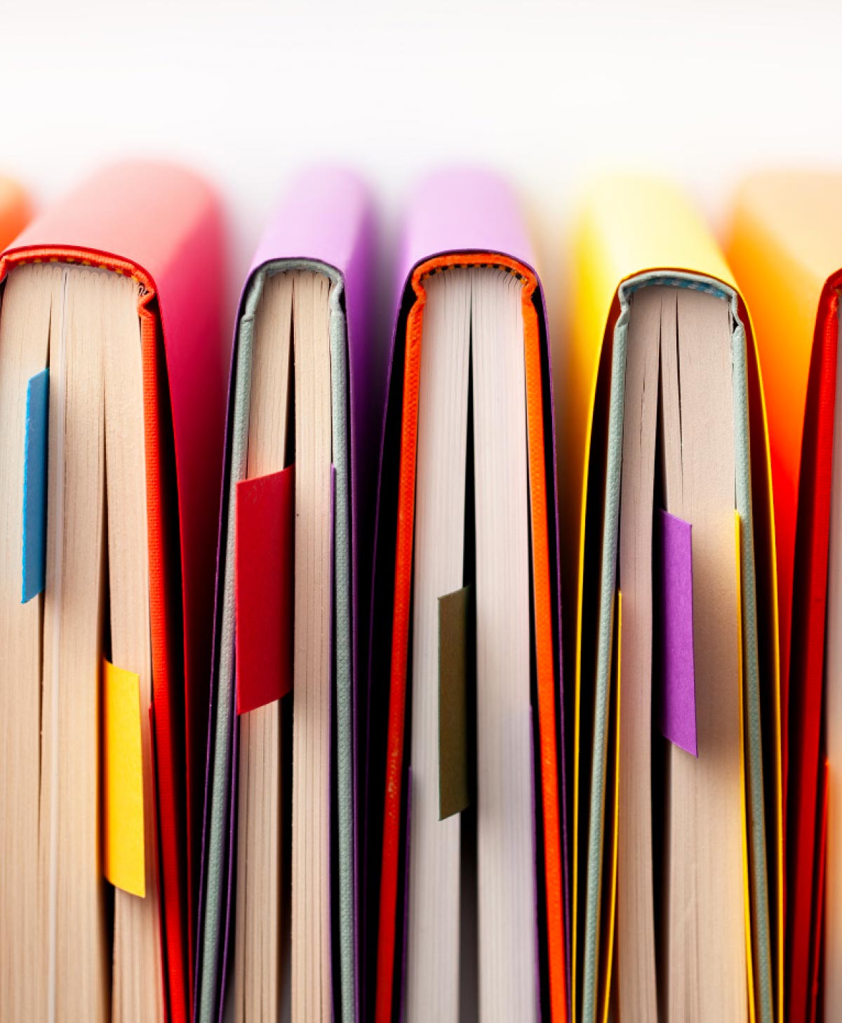 A close-up view of a row of brightly colored hardcover books standing upright with various colorful sticky note tabs bookmarking the pages.