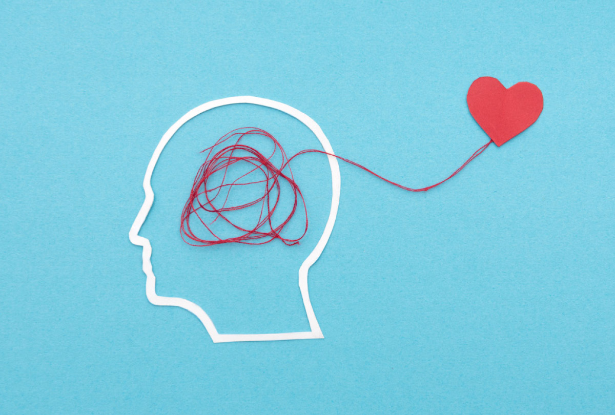 Paper cutout of a human head profile with tangled red string inside, leading out to a small red paper heart on a blue background.