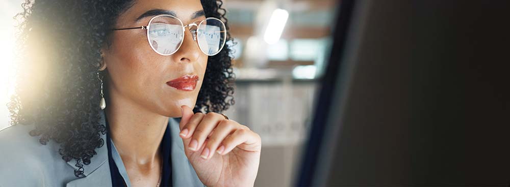 A woman with curly hair looking thoughtfully at a computer screen.