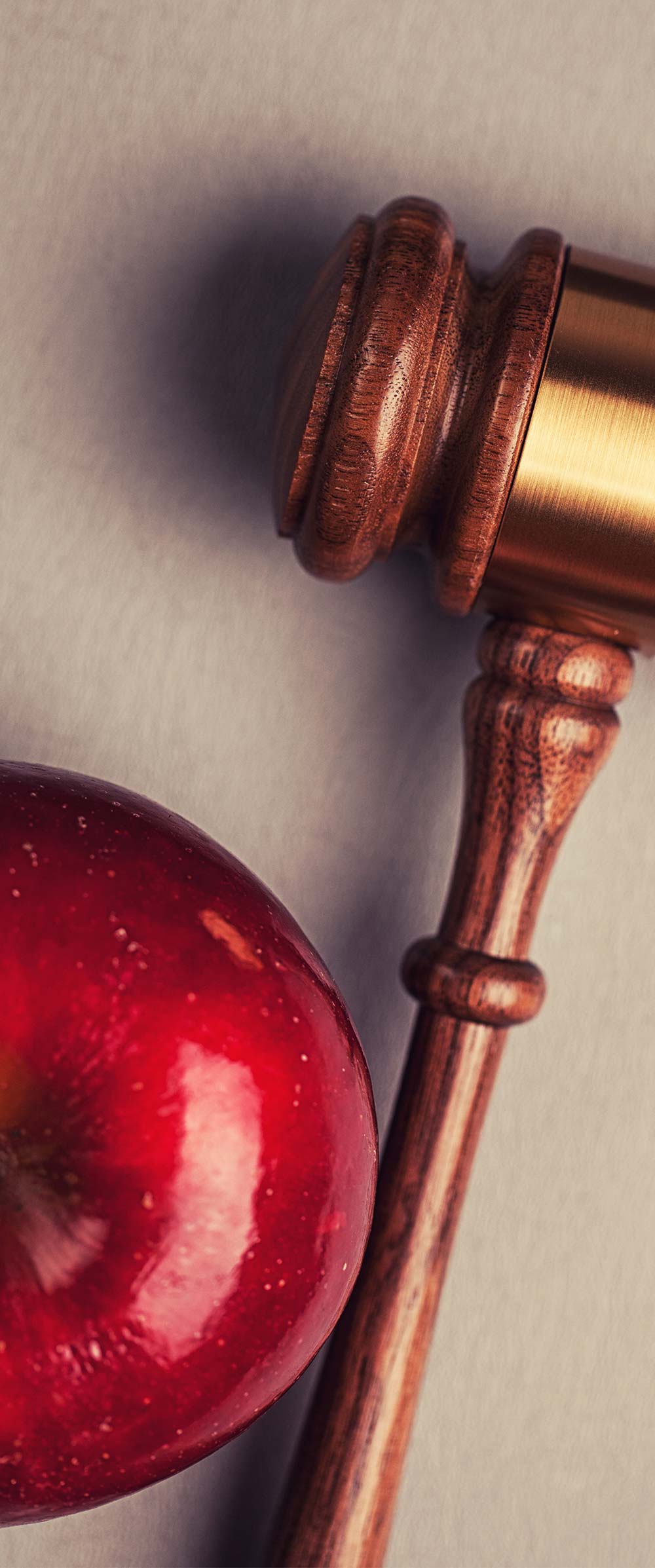 A close-up, top-down view of a shiny red apple positioned next to a wooden gavel.