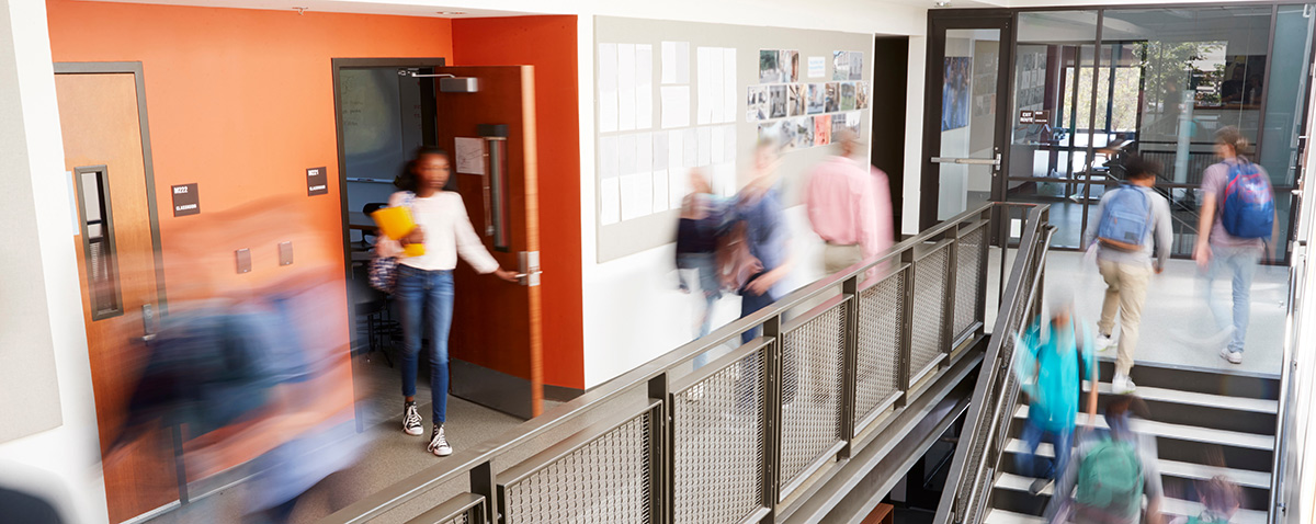 Students walk through a busy school hallway next to a staircase.