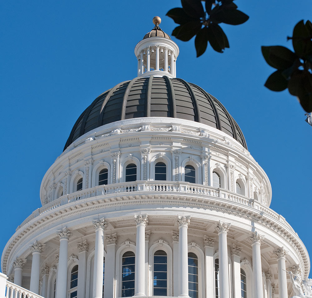 Low-angle view of the white dome and lantern of a capitol building against a blue sky.
