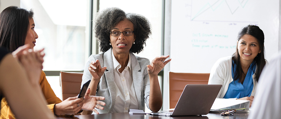 A woman gestures with her hands while leading a meeting around a conference table.