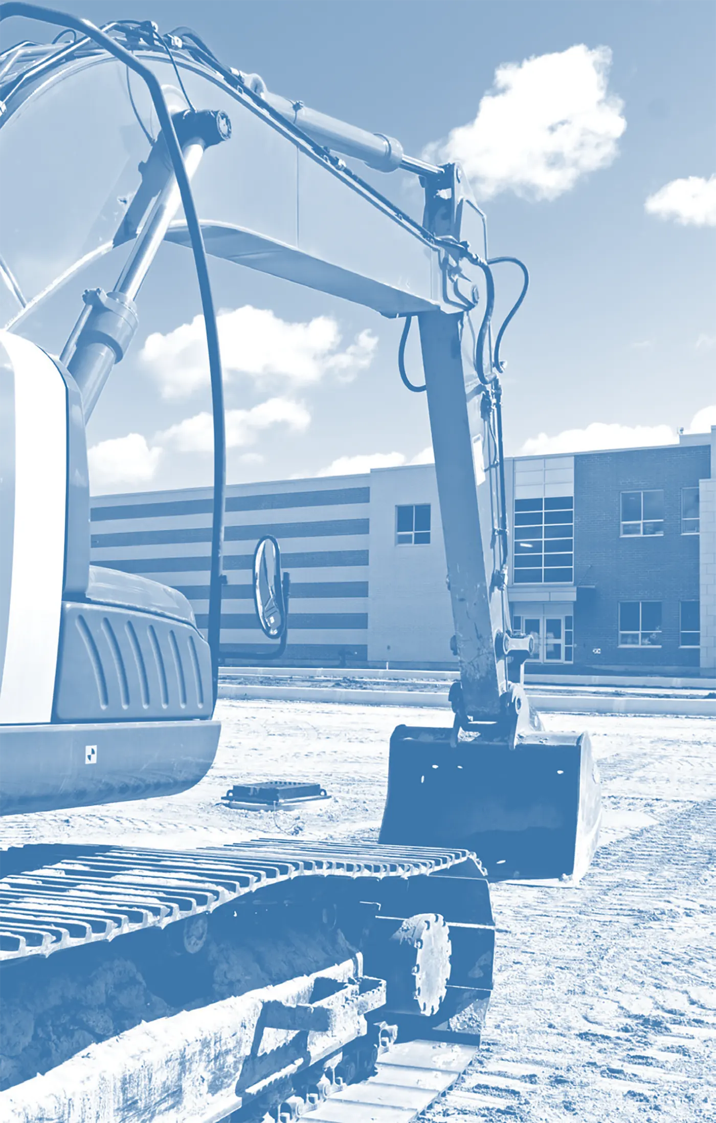 Blue-toned close-up of construction excavator tracks and arm at a construction site with a school building in the background.
