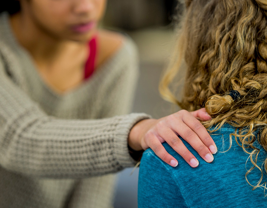 A person placing a comforting hand on another person's shoulder during a supportive conversation.