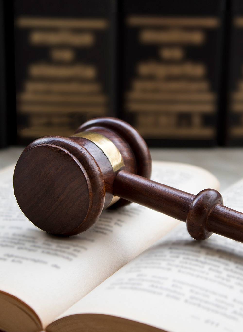 Wooden judge's gavel resting on an open book with law volumes blurred in background.